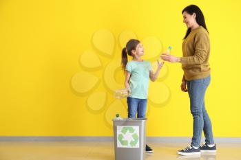Mother and daughter throwing garbage into trash bin near color wall. Concept of recycling�