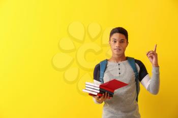 African-American schoolboy with books and raised index finger on color background�