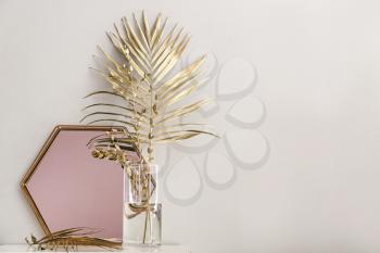 Golden tropical leaves and mirror on table near white wall�
