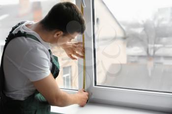 Male worker taking measurements of window in flat�