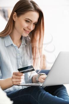 Young woman with credit card shopping online at home�