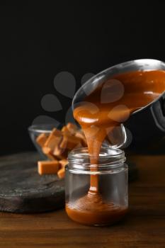 Liquid caramel pouring from pot into jar on table�