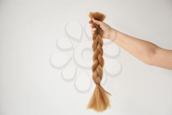 Female hand with braided strand on light background. Concept of hair donation�