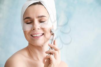 Woman with under-eye patches and facial massage tool on light background�