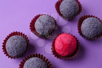 Red candy among purple ones on color background. Concept of uniqueness�