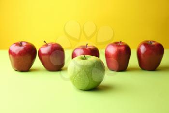Green apple among red ones on color background. Concept of uniqueness�