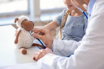 Pediatrician with toy showing little girl how to use stethoscope in clinic�