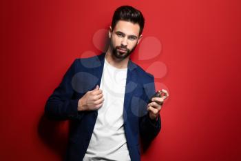 Handsome man with bottle of perfume on color background�