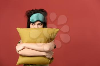 Sleepy young woman with mask and pillow on color background�
