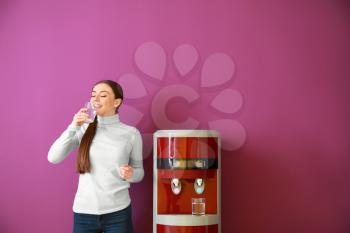 Woman drinking water from cooler against color background�