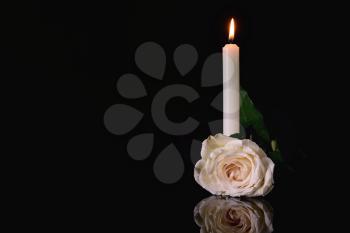 Burning candle and flower on black background�