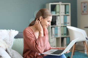 Young woman with hearing aid using laptop at home�