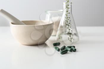 Composition with mortar, flask and plant based pills on table�