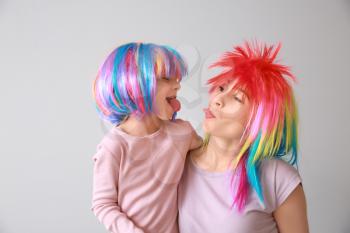 Funny little girl and her mother in bright wigs on light background. April fools' day celebration�