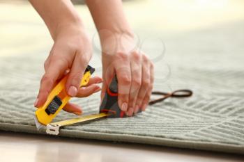Woman with tape measure cutting carpet on floor, closeup�