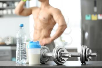 Protein shake, bottle of water and dumbbells on table�