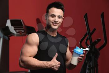 Sporty man with protein shake on color background�