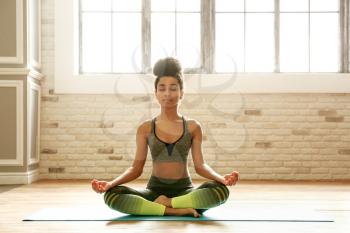 Sporty African-American woman practicing yoga indoors�