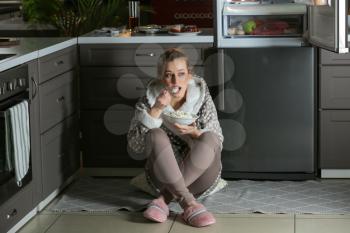 Wary woman eating food in kitchen at night�