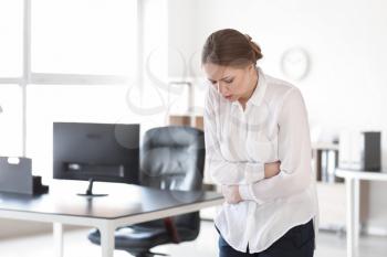 Young woman suffering from stomachache in office�
