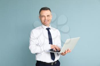 Handsome mature businessman with laptop on color background�