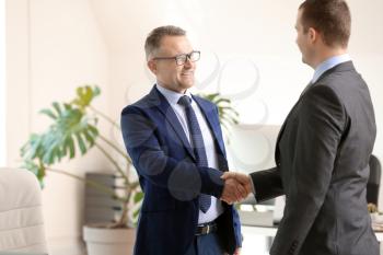 Handsome mature businessman shaking hands with client in office�