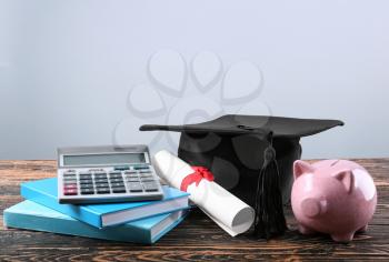 Mortar board, books, calculator, diploma and piggy bank on table. Fee-paying education concept�