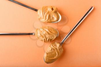 Spoons with peanut butter on color background�