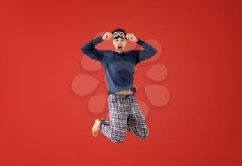 Jumping young man in pajamas with sleep mask on color background�