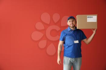 Handsome delivery man with box on color background�