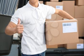 Handsome delivery man showing thumb-up near car with parcels outdoors�
