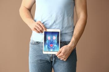 Man holding tablet computer with urinary system on screen against color background�