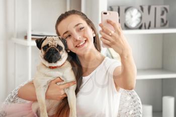 Teenage girl taking selfie with cute pug dog at home�