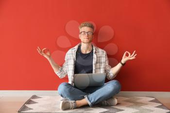 Handsome young man with laptop meditating near color wall�