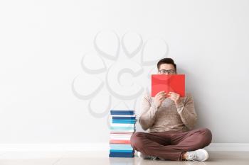 Handsome young man with books sitting near light wall�