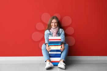 Beautiful young woman with books near color wall�
