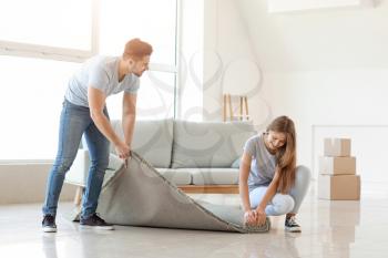 Young couple unrolling carpet on floor�