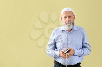 Senior Muslim man with Koran and tasbih against color background�
