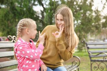 Mother teaching her deaf mute daughter to use sign language outdoors�