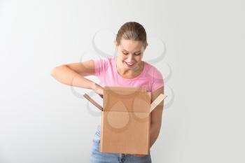 Young woman with cardboard box on light background�