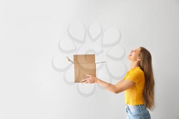 Young woman with open cardboard box on light background�