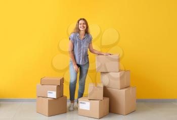 Young woman with many cardboard boxes near color wall�