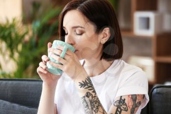 Beautiful tattooed woman drinking coffee at home�