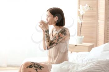 Morning of beautiful tattooed woman drinking coffee in bedroom�