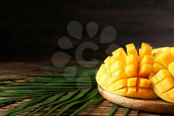 Plate with tasty fresh mango and tropical leaves on wooden table�