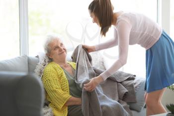 Caregiver covering senior woman with plaid in nursing home�