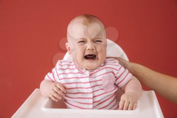 Crying little baby sitting in chair against color background�