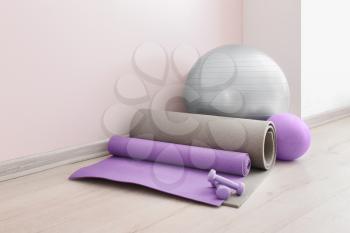 Set of sports equipment with fitness ball near light wall�