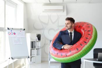 Handsome businessman with inflatable ring in office. Travel concept�