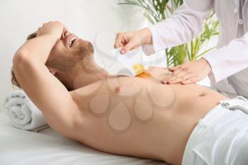 Young man suffering from pain during epilation in beauty salon�